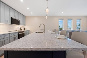 A modern kitchen with a granite countertop, stainless steel appliances, and a large window providing a view of the outdoors. - Salty Seahorse Unit 100 (Fort Myers Beach)