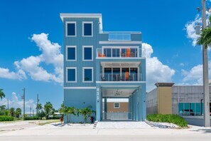A multi-story building with a flat roof, large windows, and a balcony with orange chairs. - Salty Seahorse Unit 100 (Fort Myers Beach)
