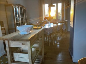 Een houten eettafel met een geruit tafelkleed, omringd door stoelen. Op de tafel staat een grote glazen schaal, en op de achtergrond een kast met glazen deuren.