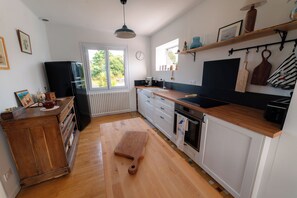 A kitchen with wooden cabinets, a stove, a sink, and a window with a view of greenery. - House for 4 people near the GR34 – Pink Granite Coast – near Perros-Guirec (Trélévern)