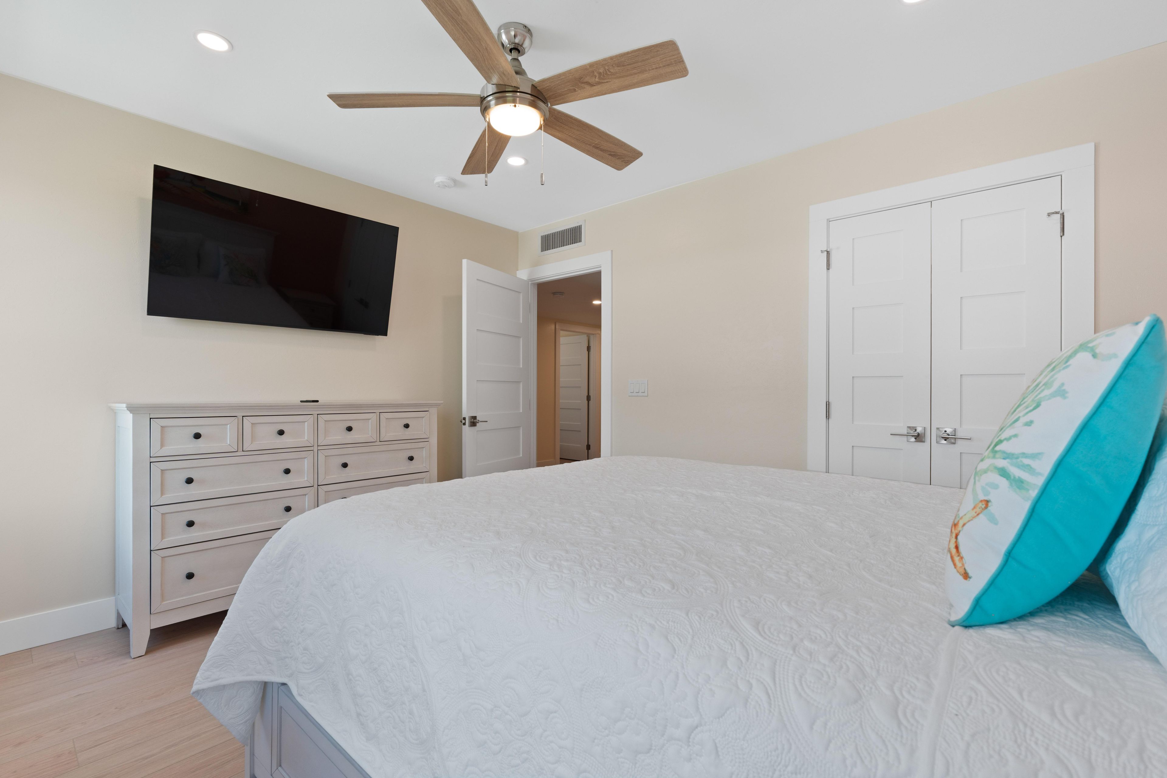 Un dormitorio con cama, cómoda, ventilador de techo y televisor montado en la pared.