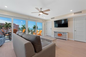 A spacious living room with a large sofa, a flat-screen TV, and a ceiling fan. - Salty Seahorse Unit 200 (Fort Myers Beach)