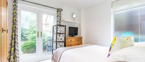 A bedroom with a bed, a television on a wooden dresser, and a sliding glass door leading to a garden.