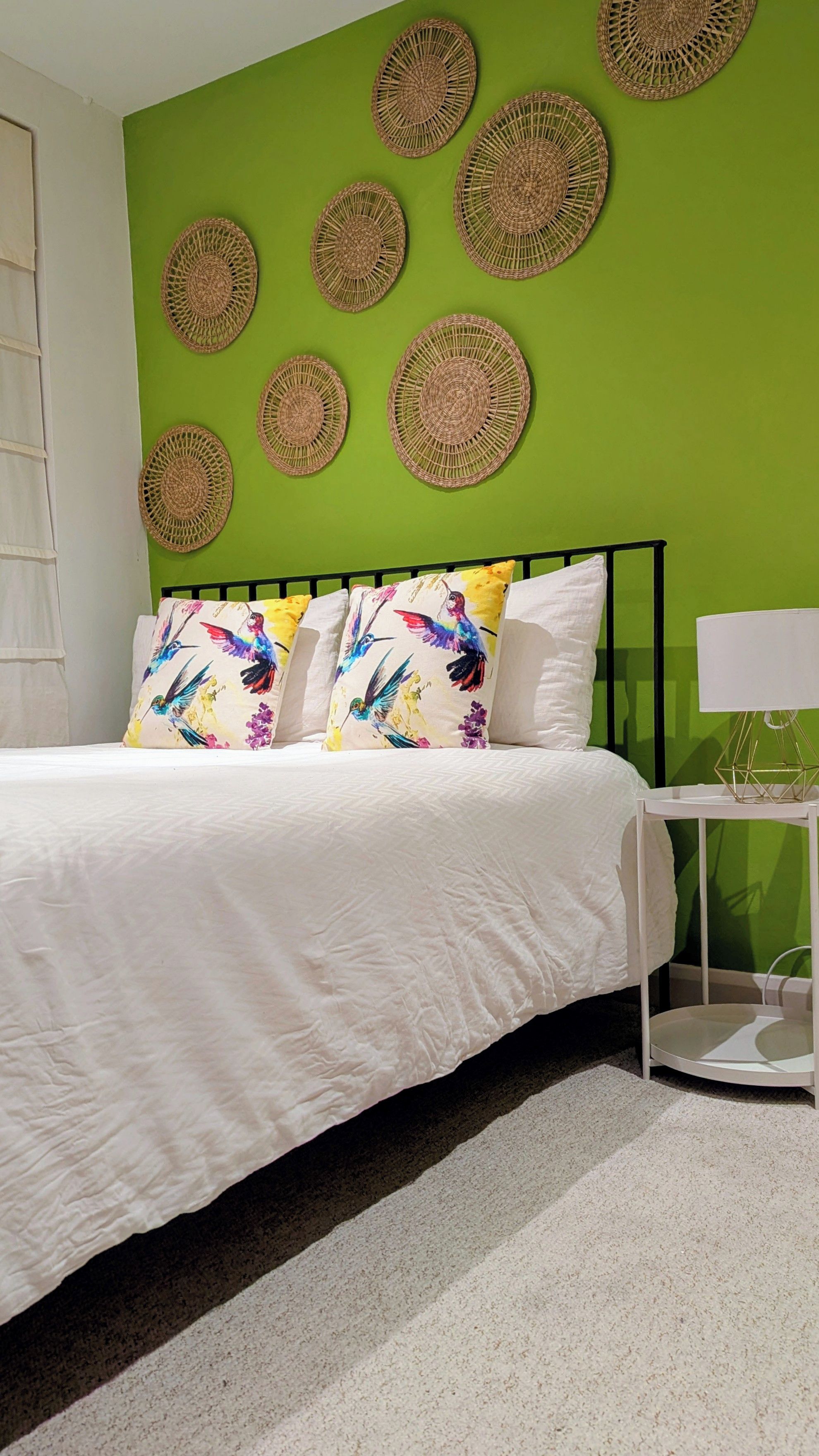 Una camera da letto con una parete verde, un letto bianco e tappetini decorativi in fibra.