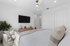 A modern bedroom with a bed, a TV, a dresser, and a potted plant. - Calico Jack's Lookout (Fort Myers Beach)