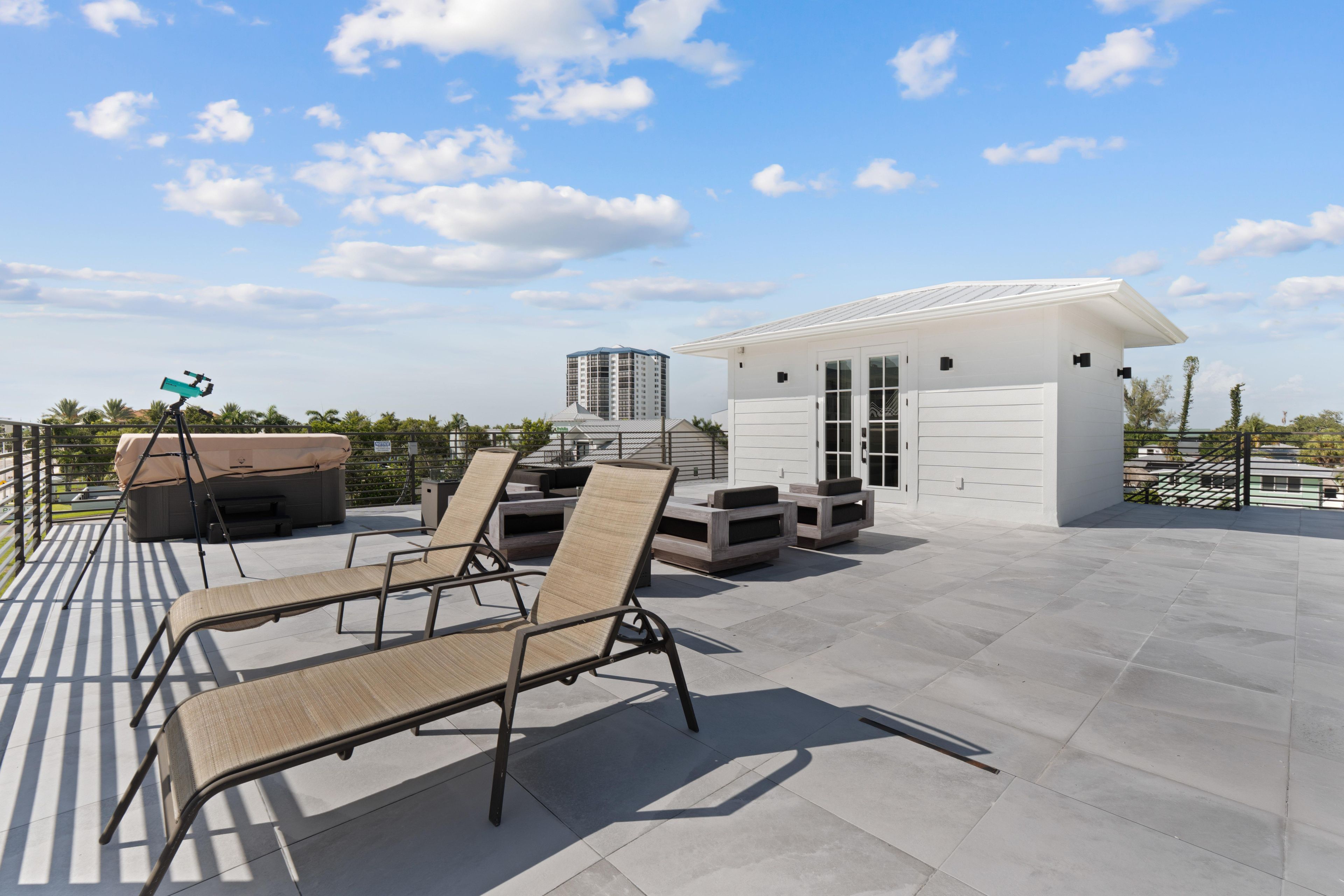 A rooftop terrace with lounge chairs, a telescope, and a small building with a white facade.