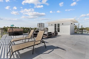 A rooftop terrace with lounge chairs, a telescope, and a small building with a white facade. - Calico Jack's Lookout (Fort Myers Beach)
