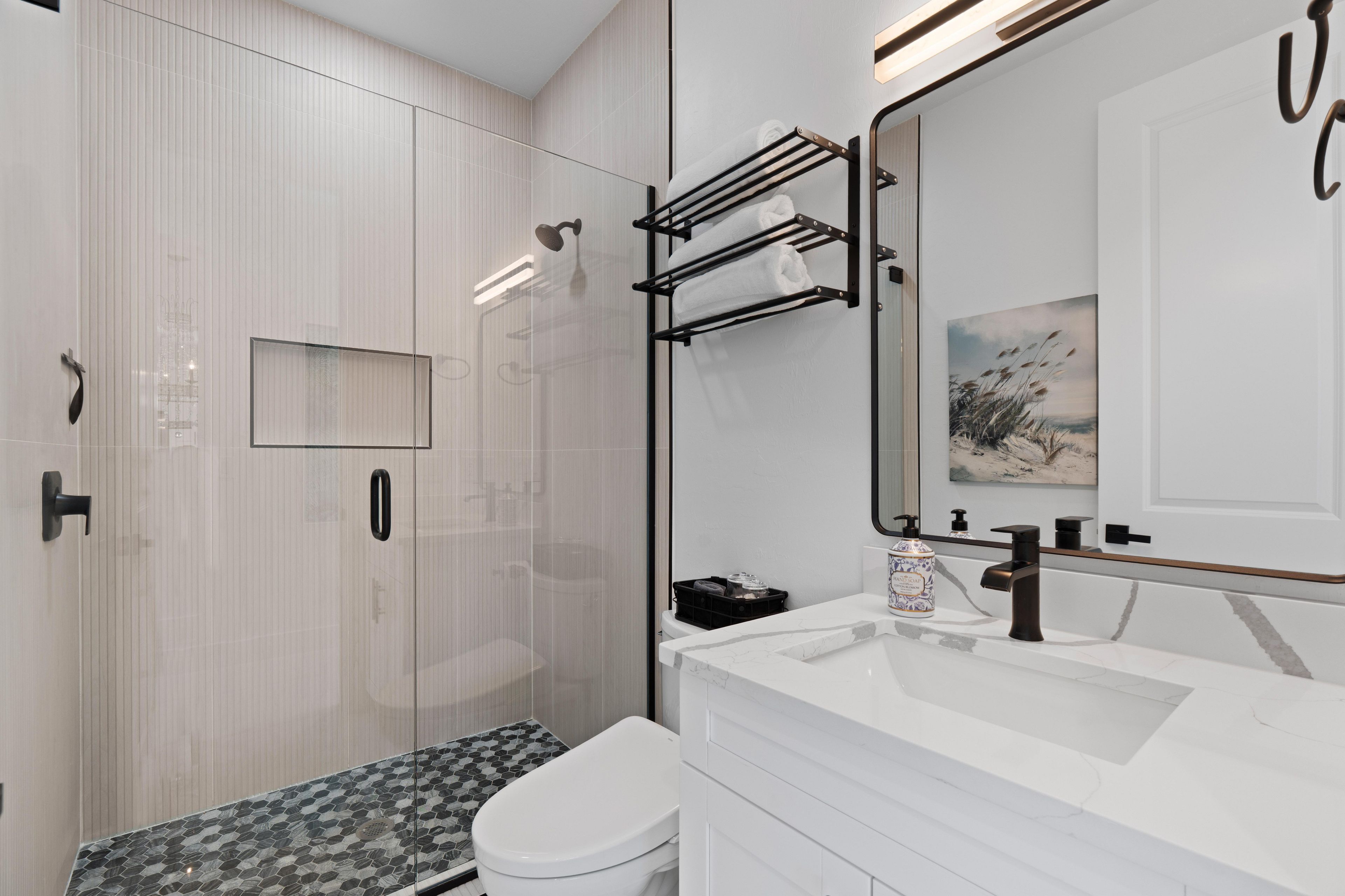 A modern bathroom with a glass shower enclosure, a white toilet, a marble sink, and a towel rack.