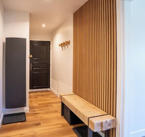 Un couloir avec un banc, une porte et un mur composé de lattes de bois verticales.