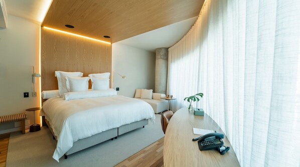 A modern hotel room with a large bed, a desk with a telephone, and a view of the outside through sheer curtains. - V3rso Nilo Square (Porto Alegre)