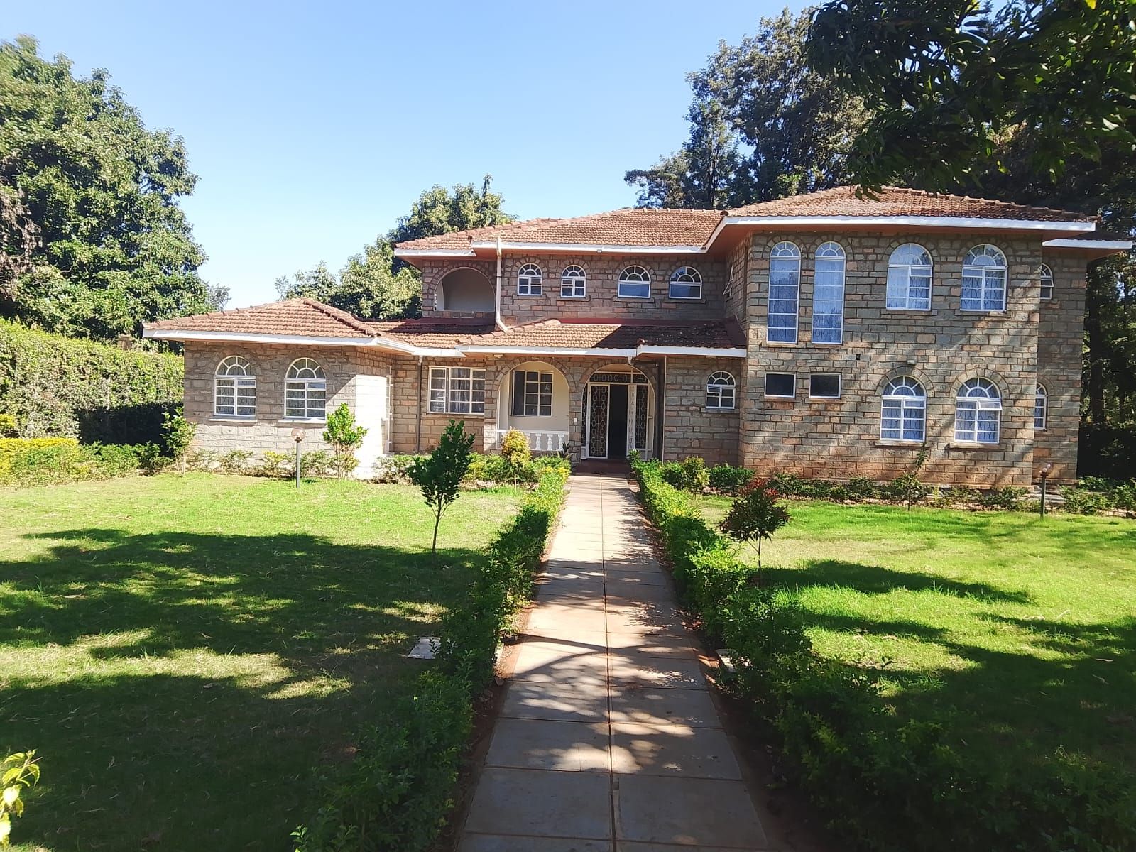 A two-story stone house with a central entrance, a covered porch, and a well-maintained lawn.