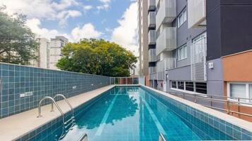 Piscina com grades de metal, parede revestida e uma árvore ao fundo.