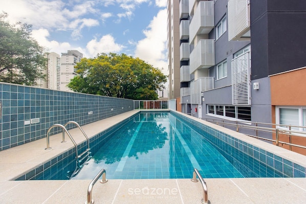 A swimming pool with metal railings, a tiled wall, and a tree in the background.