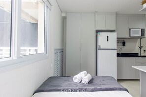 Quarto compacto com cama, pequeno espaço de cozinha e janela.