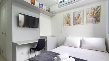 Quarto de hotel com cama, secretária, cadeira, televisão e três obras de arte emolduradas na parede.