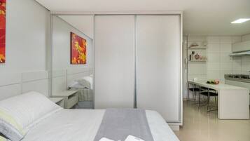 Quarto de hotel moderno com uma cama, uma secretária pequena e uma cozinha compacta.
