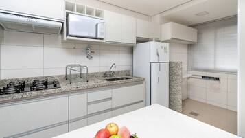 Uma cozinha moderna com armários brancos, bancada de granito, micro-ondas, pia e geladeira.