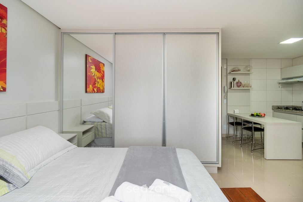 A modern hotel room with a bed, a small desk, and a kitchenette.