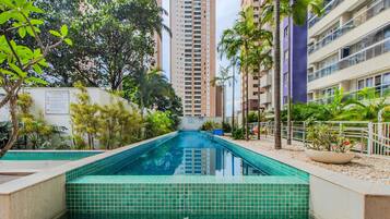 Piscina cercada por vegetação e edifícios altos.