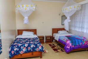 A bedroom with two beds, each with a canopy, a nightstand, and a patterned rug. - Royal Gardens Muthatari - Embu : Standard Double Room with Two Double Beds (Embu)
