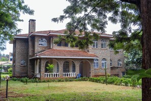 A two-story stone house with a tiled roof, a covered porch with a white balustrade, and a well-maintained lawn.