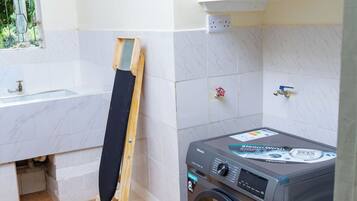 A laundry area with a washing machine, a drying rack, and a window with a view of greenery.