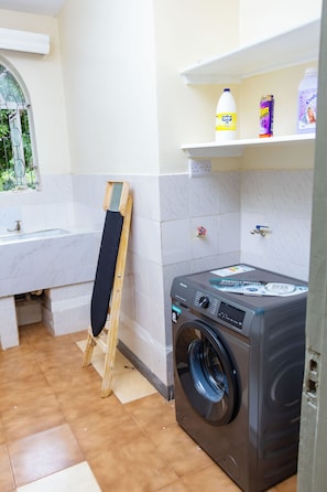 A laundry area with a washing machine, a drying rack, and a window with a view of greenery.