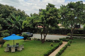A well-maintained garden with a paved walkway, a seating area with a blue umbrella, and a parked car. - Royal Gardens Muthatari - Embu : Deluxe Twin Room (Embu)
