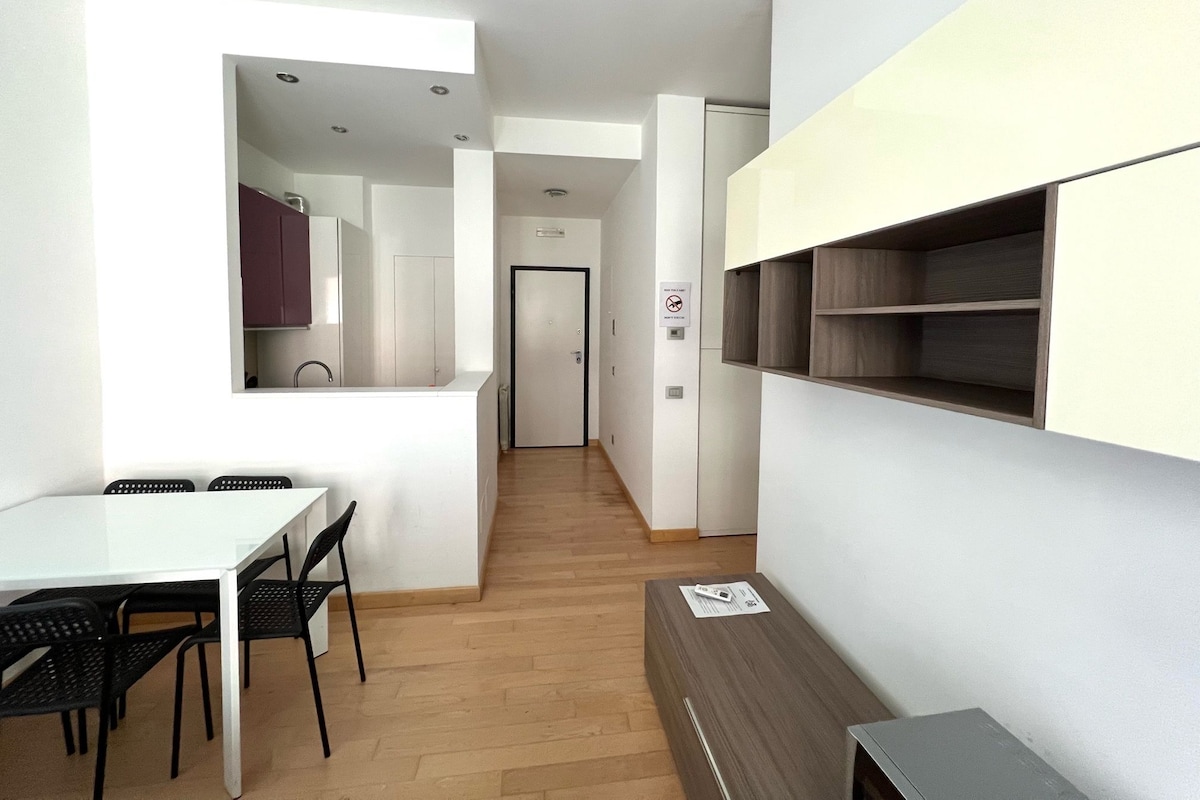A modern kitchen with white cabinets, a dining area with a white table and black chairs, and a hallway leading to a door.