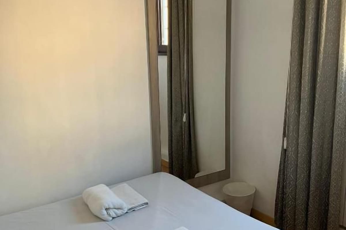 A hotel room with a bed, two towels, a mirror, and a curtain.