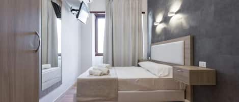 Quarto moderno com cama, mesa de cabeceira e televisão presa na parede.