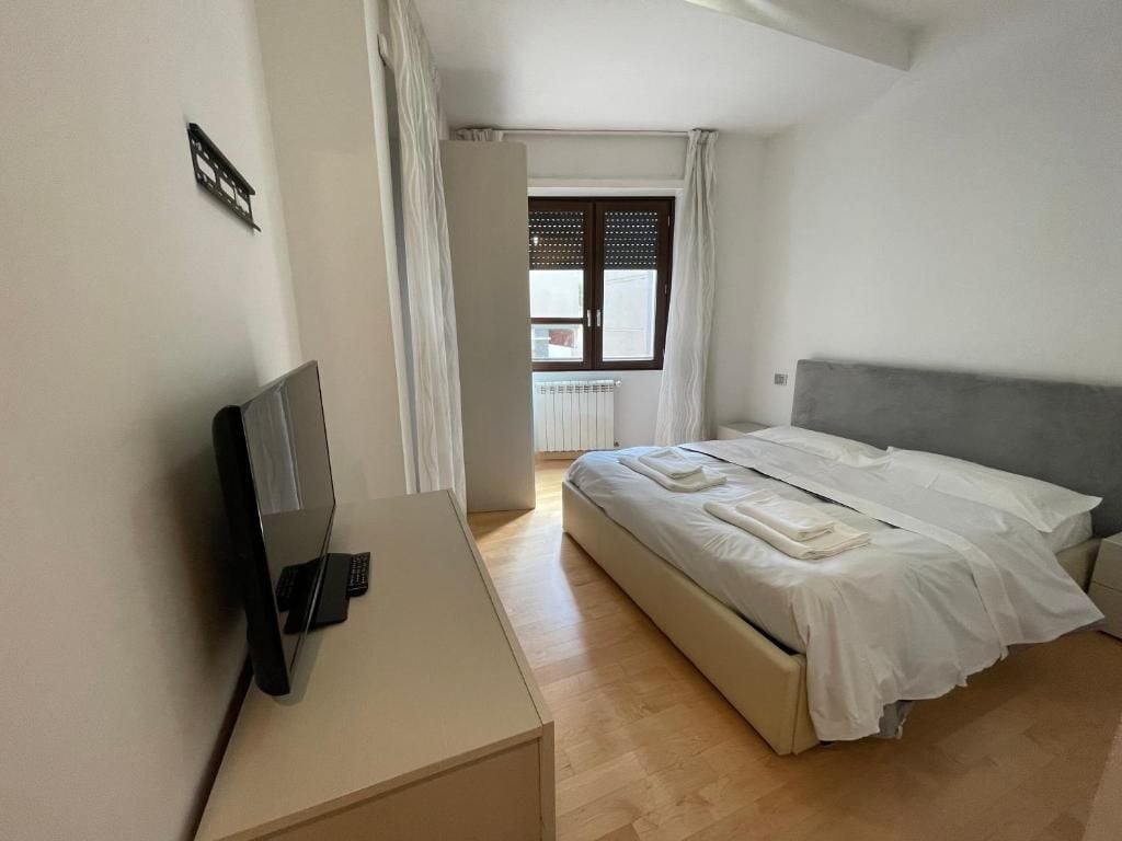 A bedroom with a bed, a desk with a laptop, a window with curtains, and a radiator.