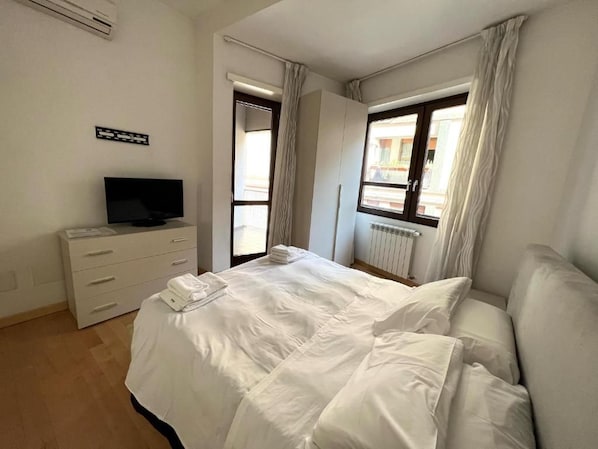 Un dormitorio con cama, televisor, cómoda y ventana con cortinas.