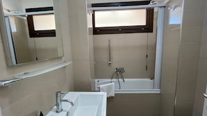 A bathroom with a bathtub, a sink, a mirror, and a window.