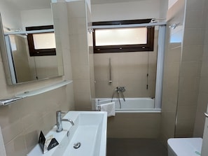 A bathroom with a bathtub, a sink, a mirror, and a window.
