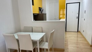 A dining area with a white table and chairs, a kitchen with yellow cabinets, and a door leading to another room.