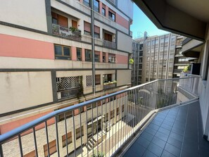 Un edificio residencial de varios pisos con balcones, piso de baldosas y baranda de metal.