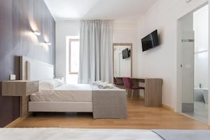 A modern bedroom with a bed, bedside tables, a desk, a chair, a television, and a bathroom visible through an open door.