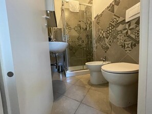 Un baño con dos inodoros, un lavamanos y cabina de ducha.