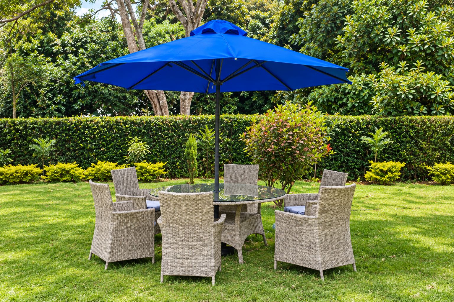 A round glass table with wicker chairs and a blue umbrella in a well-maintained garden.