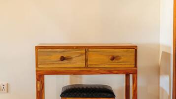 A wooden desk with two drawers and a bench, set against a plain wall with a thatched ceiling.