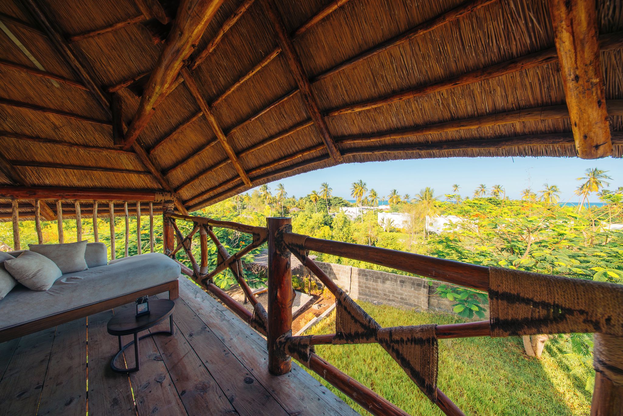A wooden deck with a thatched roof, a sofa, and a table.