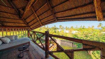 A wooden deck with a thatched roof, a sofa, and a table.