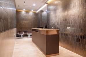 Zona de recepción de diseño moderno, con mostrador, dos sillas y una pared con líneas verticales.
