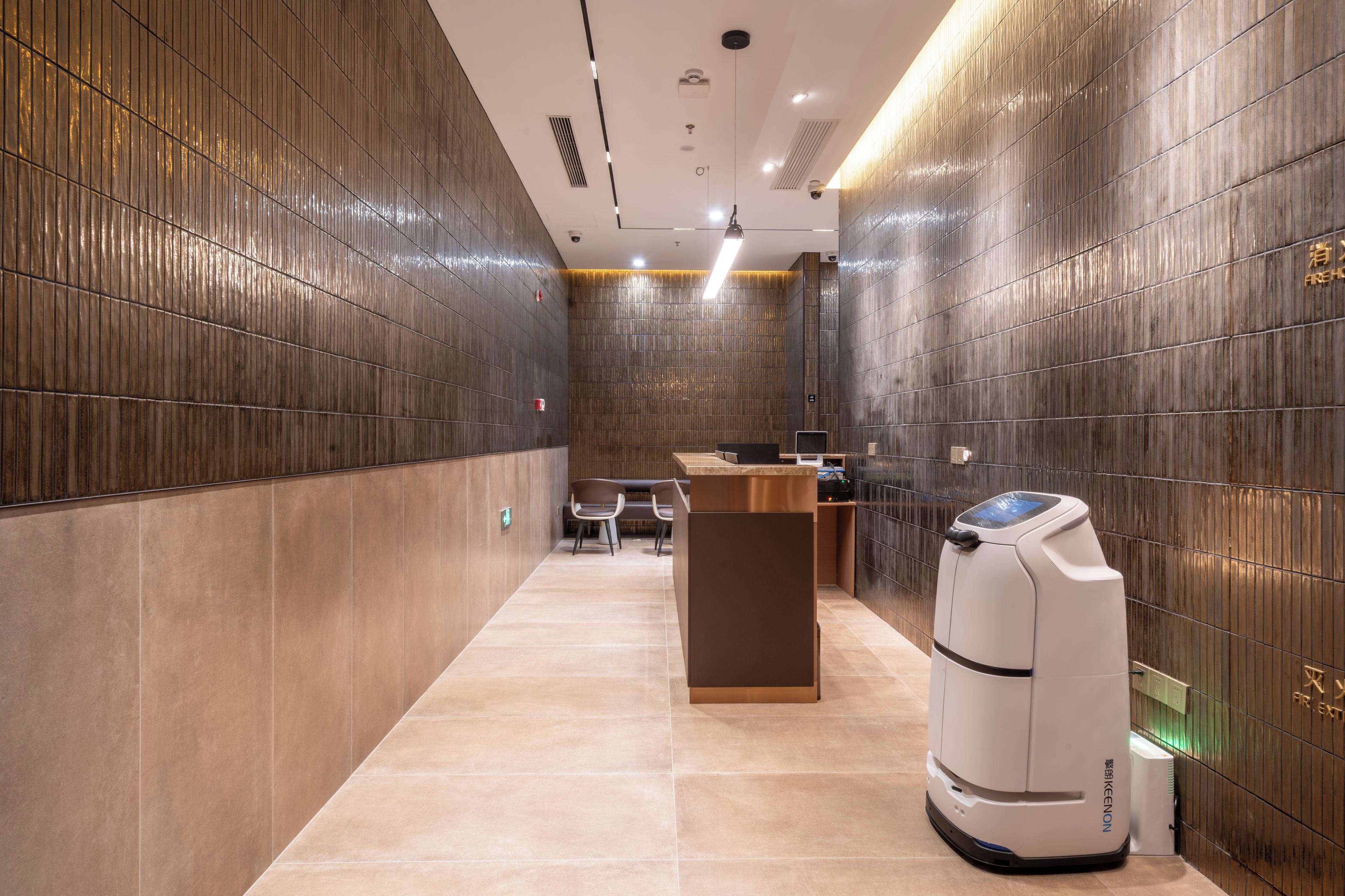 A modern hotel lobby with a reception desk, seating area, and a self-service kiosk.