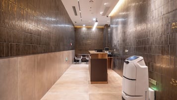 Um lobby de hotel moderno com balcão de recepção, área de estar e um quiosque de autoatendimento.