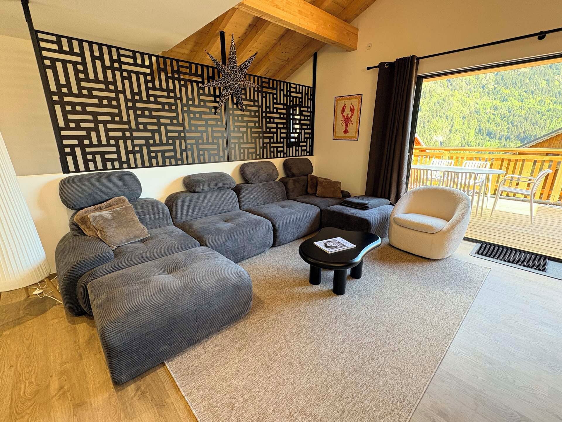 Ein modernes Wohnzimmer mit einem Ecksofa, einem kleinen schwarzen Couchtisch und einem weißen Sessel. Eine dekorative Wandverkleidung und ein gerahmtes Kunstwerk sind zu sehen.