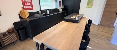 A modern kitchen with a central island, black cabinetry, and a dining area with a long wooden table and black chairs.