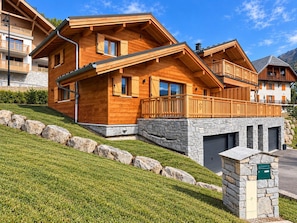 Un chalet en bois avec des fondations en pierre, une boîte aux lettres en pierre et une pente herbeuse.