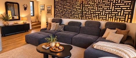 Una sala de estar moderna con un sofá modular, una mesa de centro con objetos decorativos, un separador de ambientes con diseño y un techo de madera.